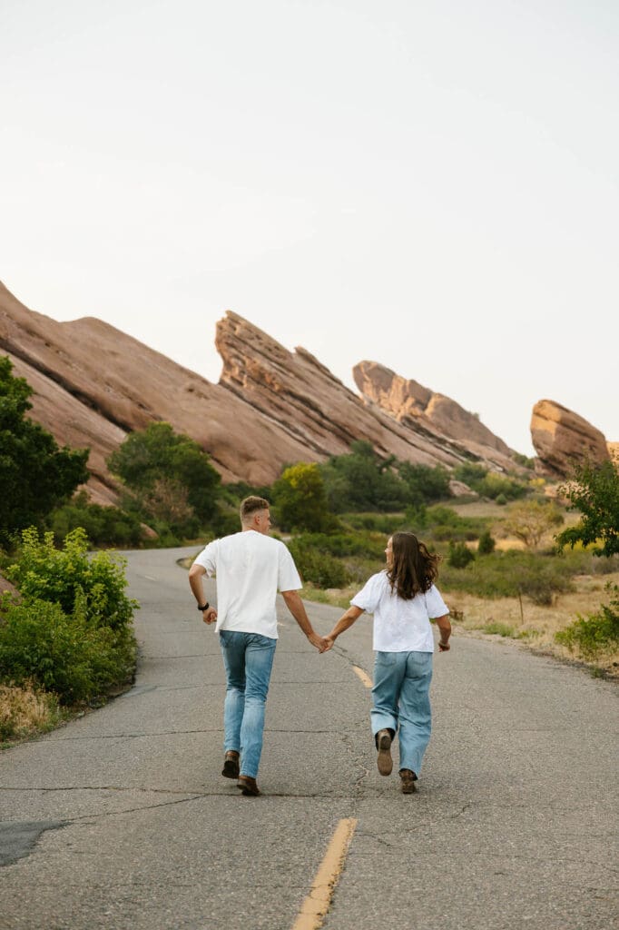 Jordan and Andrew running hand in hand down a road during their Red Rocks engagement session
