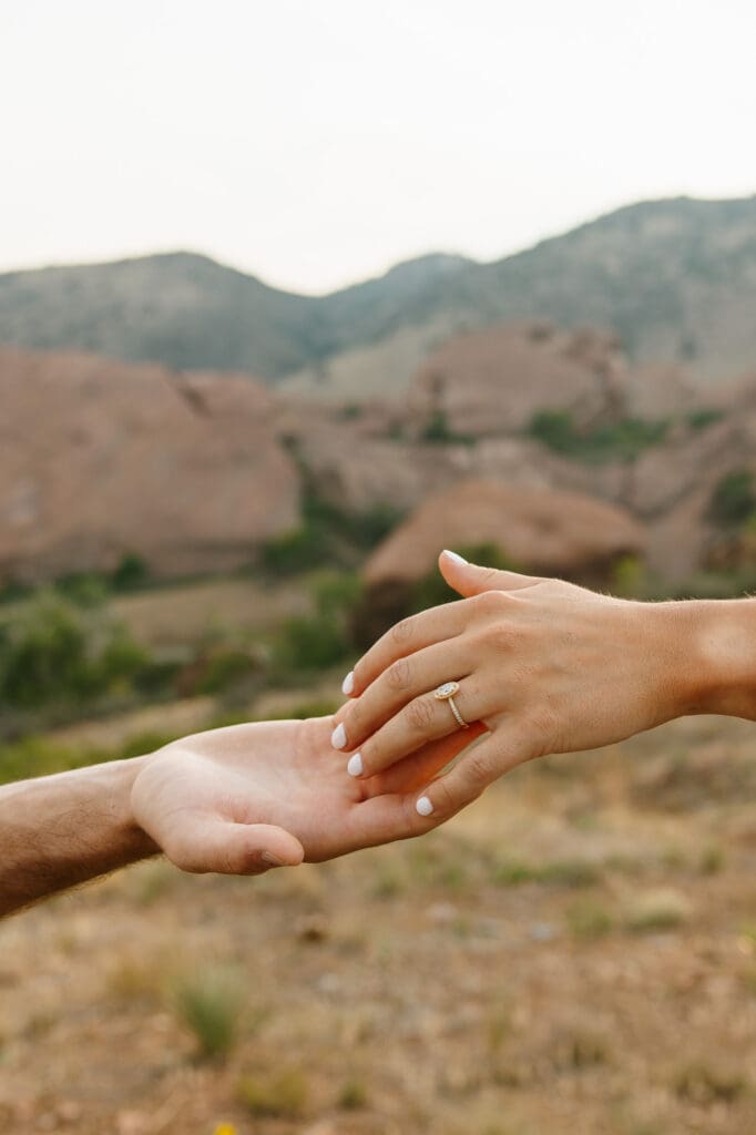 Close-up of Jordan and Andrew holding hands with Jordan's engagement ring and Red Rocks in the background